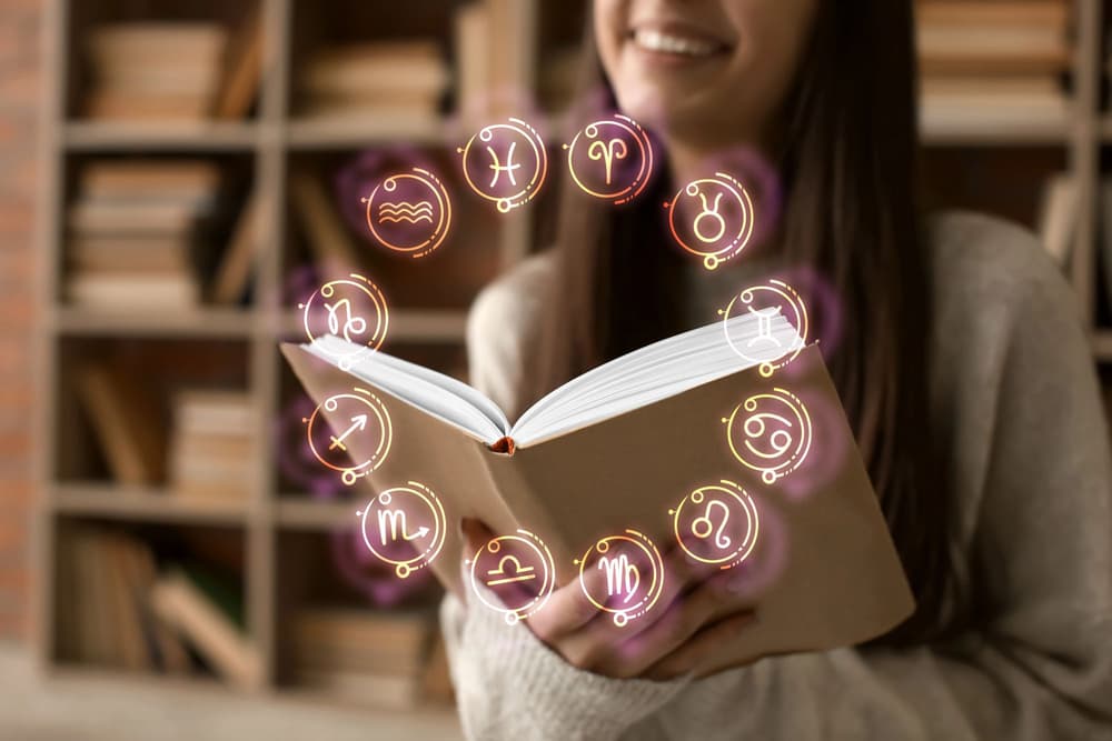 uśmiechnięta kobieta czytająca książkę o znakach zodiaku 