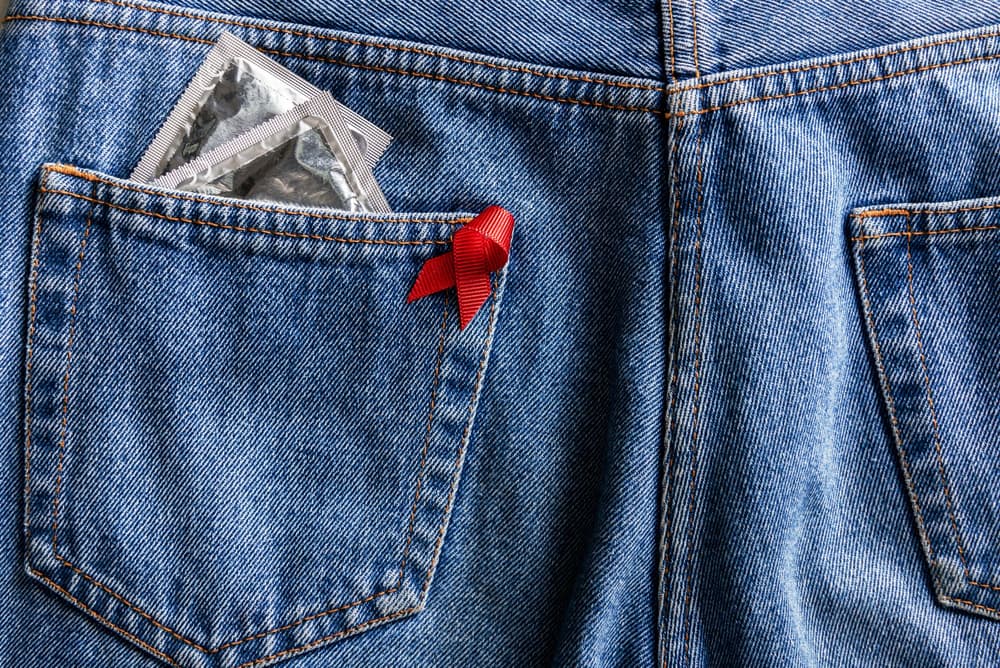 czerwona kokardka oznaczająca wirusa HIV i prezerwatywy w kieszeni czerwona kokardka oznaczająca wirusa HIV i prezerwatywy w kieszeni
