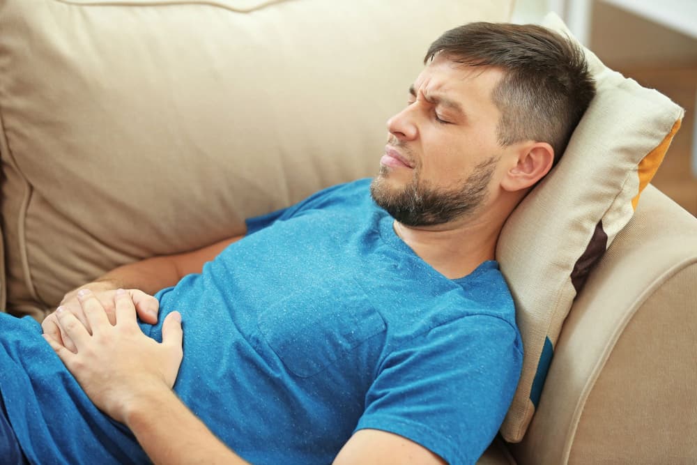 mężczyzna leżący na łóżku z bólem brzucha mężczyzna leżący na łóżku z bólem brzucha