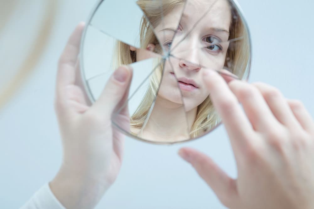 kobieta wpatrująca się w popękane lusterko kobieta wpatrująca się w popękane lusterko