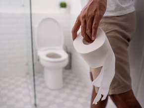 Mężczyzna korzystający z toalety i trzymający w dłoni papier toaletowy.