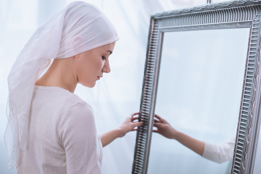 Młoda kobieta chora na raka patrząca w lustro.