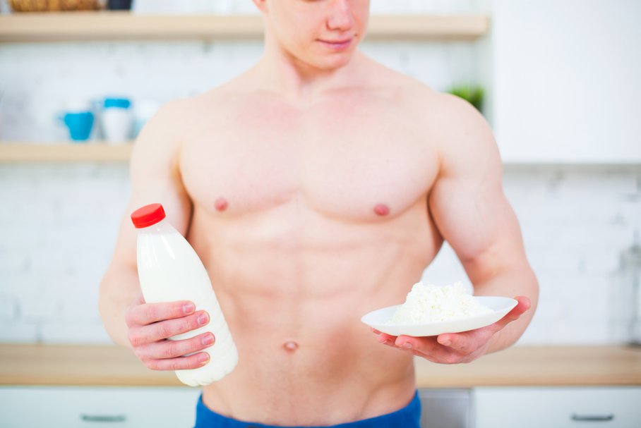 Młody umięśniony mężczyzna w kuchni trzymający w dłoniach butelkę mleka i talerz twarogu.