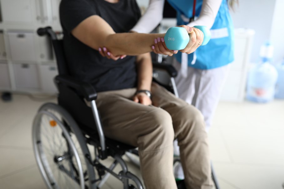 Mężczyzna na wózku inwalidzkim podczas ćwiczeń z fizjoterapeutką.