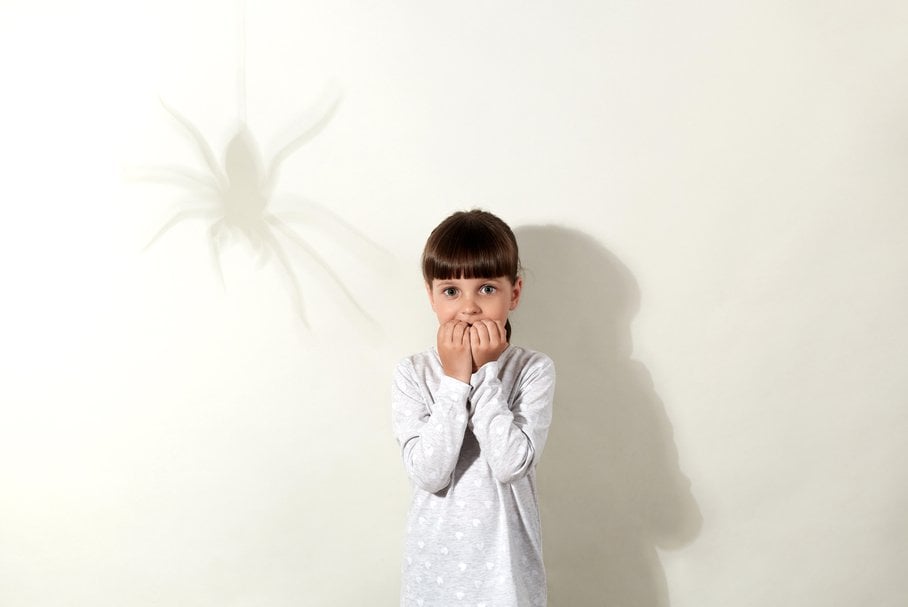 Przestraszona dziewczynka obok cienia pająka na ścianie.
