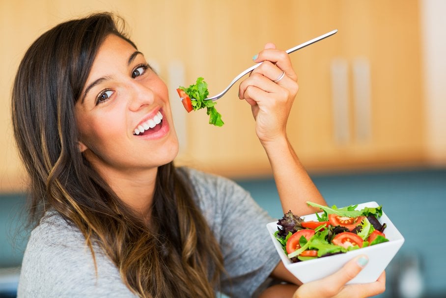 Uśmiechnięta młoda kobieta jedząca sałatkę.