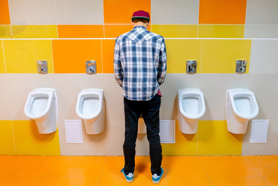 Mężczyzna oddający mocz w publicznej toalecie.