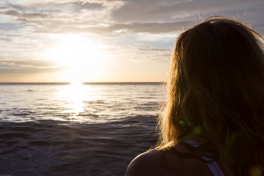 Kobieta patrząca na słońce nad morzem.