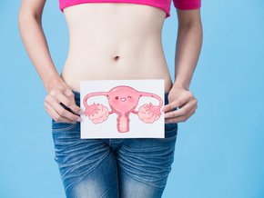Młoda kobieta trzymająca kartkę z grafiką przedstawiającą uśmiechnięty żeński układ rozrodczy.