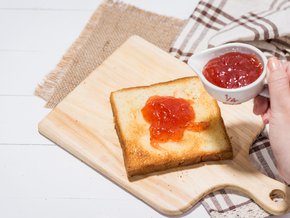 Kobieta nakładająca dżem na kromkę pieczywa tostowego.