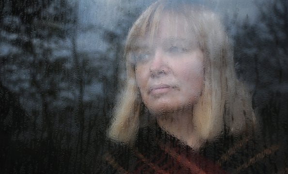 Smutna kobieta wyglądająca przez okno.