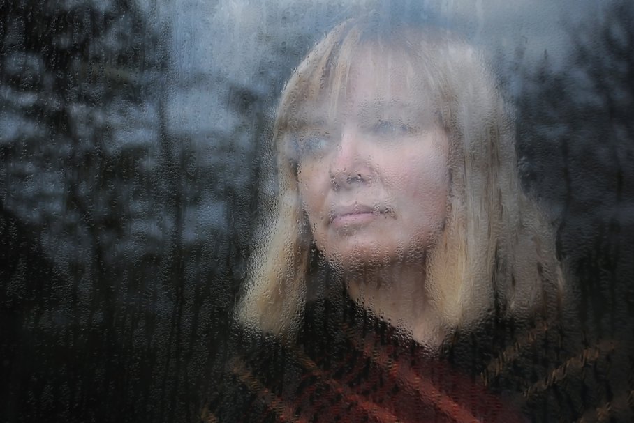 Smutna kobieta wyglądająca przez okno.