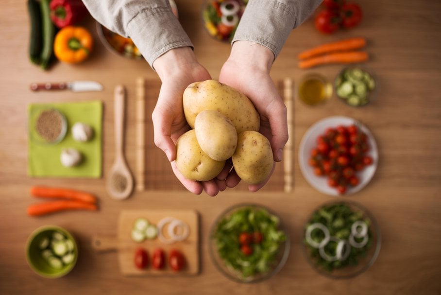 Osoba trzymająca w dłoniach ziemniaki nad stołem warzyw.