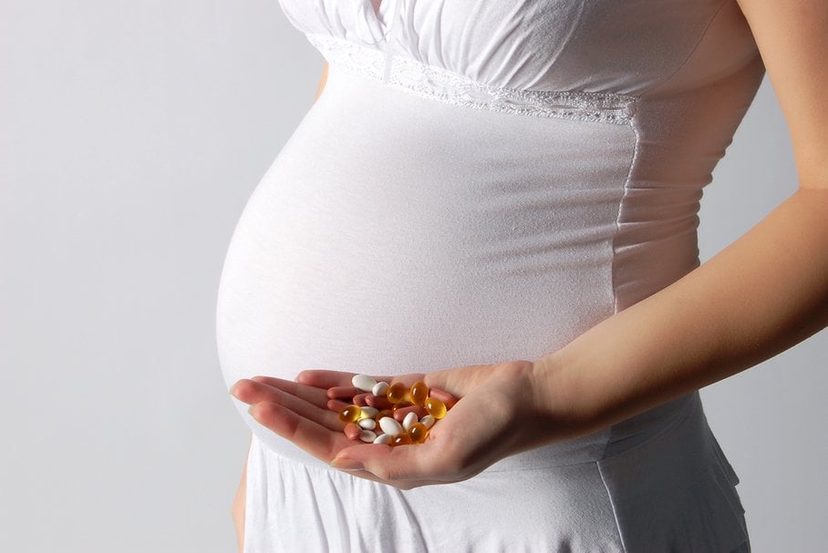 Kobieta w ciąży trzymająca garść tabletek.
