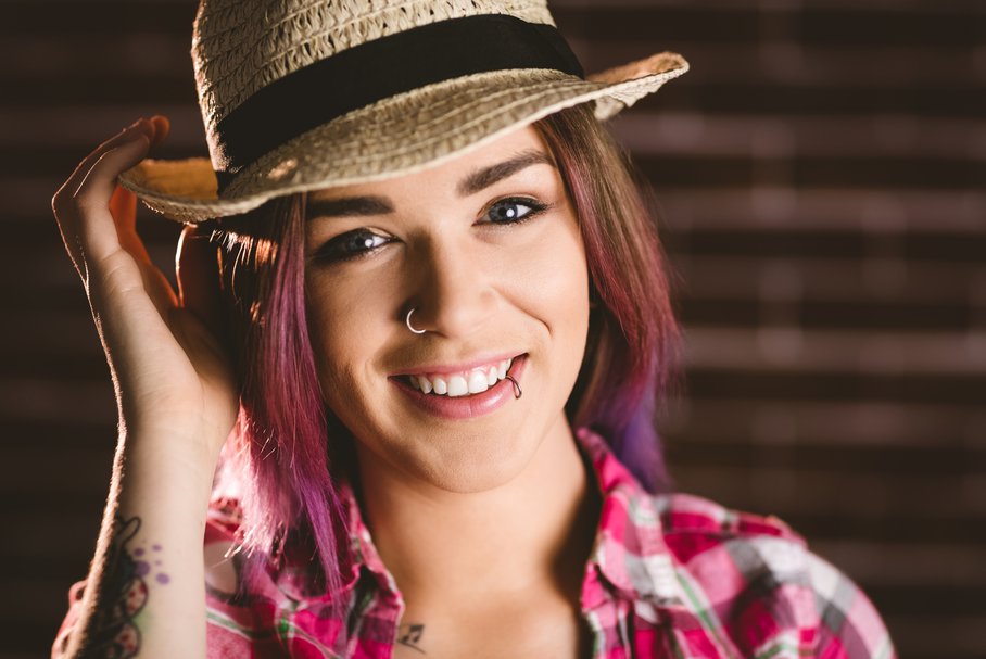Uśmiechnięta młoda kobieta w kapeluszu i z piercingiem.