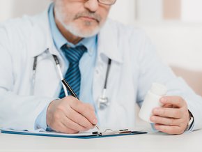 Lekarz trzymający opakowanie leku i robiący notatki.