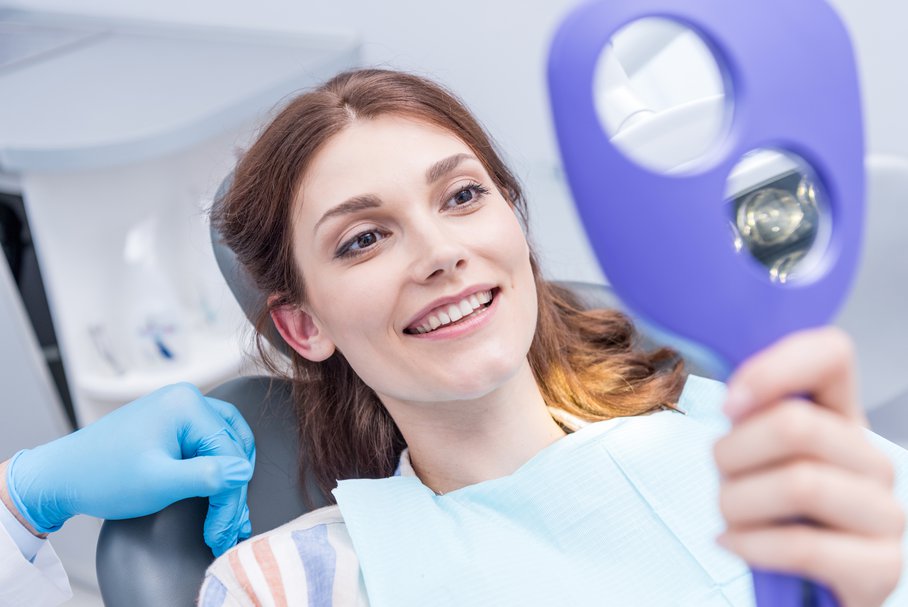 Kobieta u dentysty oglądająca swoje zęby w lustrze.