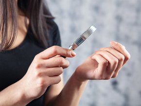 Kobieta oglądająca paznokcie rąk z pomocą szkła powiększającego.
