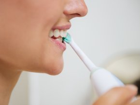 Kobieta myjąca zęby szczoteczką soniczną.