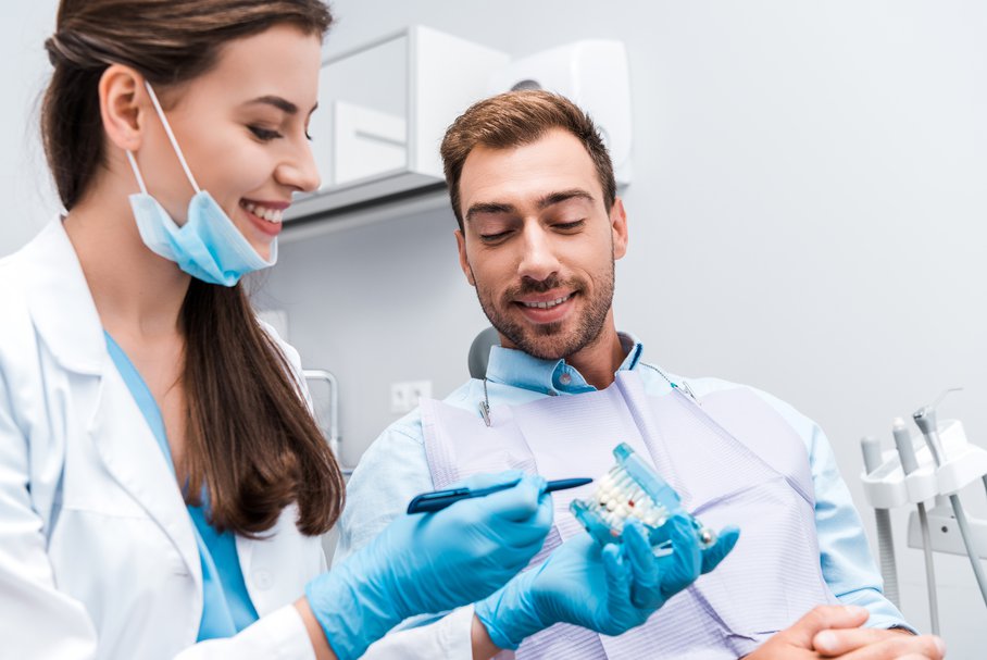 Uśmiechnięta stomatolog pokazująca pacjentowi model szczęki.