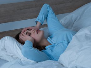 Kobieta w łóżku cierpiąca na ból głowy.