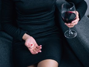 Kobieta w czarnej sukience pijąca wino i zażywająca tabletki.