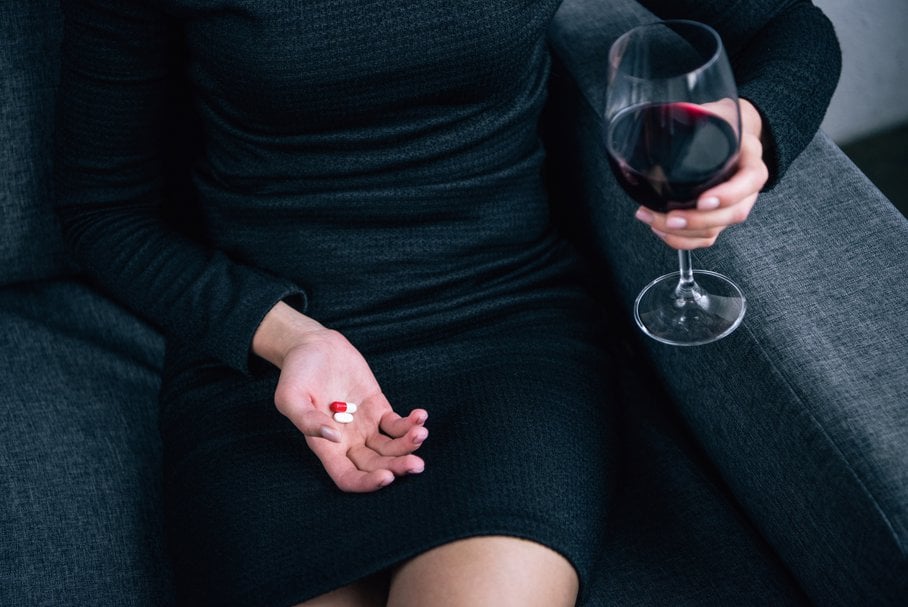 Kobieta w czarnej sukience pijąca wino i zażywająca tabletki.